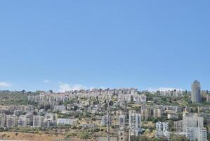 A panoramic view of hillside residential buildings stacked along green slopes, with blue sky creating a peaceful urban landscape photo