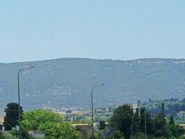 Green-covered mountains stretch across the horizon, with lamp posts and urban vegetation below under a clear summer sky photo