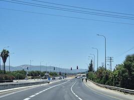 A wide open highway with traffic lights and clear skies, surrounded by greenery and distant hills under bright sunlight photo