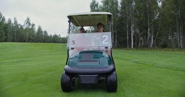Men of European appearance with a big age difference are driving a golf car on a golf course and talking to each other on a rainy cloudy day, front view photo