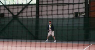 The young man of European appearance plays big tennis, hitting the ball with a racket over and over again, bouncing with each racket hit, filming through the net, the drawing of the net is visible photo