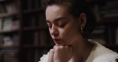 A beautiful girl of European appearance with freckles and in large earrings is thinking intently, resting her chin with her hands and looking down at the table, close-up photo