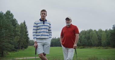 Two men of different ages are leaning on golf clubs on the golf course and smiling while looking at the camera photo