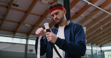 A young man of European appearance wraps the handle of a tennis racket with a special tape, for better grip with his hand, preparing for a tennis match, close up photo