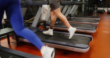 Young man and woman, dressed in stylish sportswear, run on a treadmill, working out in a modern gym together. Moving from a close up of the legs to a general view of the athletes photo