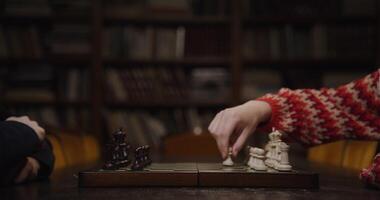 A man and a woman start a chess game, sitting opposite each other at a table in the library, close up of a chessboard photo