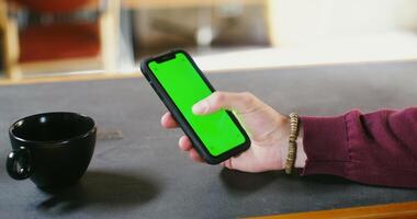 A man uses a phone with a green screen while sitting at a table. Male hand close up, copy space, chroma key. photo