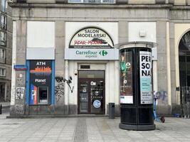Warsaw, Poland - May 22, 2025 Jadar Model Salon storefront featuring Carrefour Express signage, ATM, and urban street art, showcasing a vibrant city atmosphere with commercial elements photo