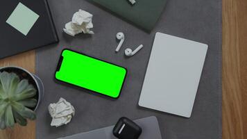 A man's hand lies on a blank sheet of a notebook, next to a mobile phone with a green screen and crumpled sheets of paper, close up. Mockup, chroma key, copy space photo