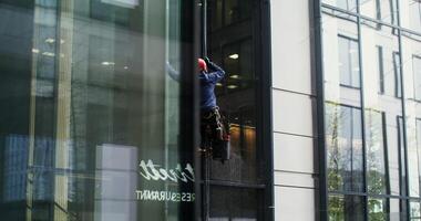 A man in a protective helmet and gear hanging from protective cables washes the windows from the outside of a high rise building, close up. in 4k, red komodo photo