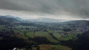 Vew of mountain valley with city in a lowland at foot of gently sloping mountains overgrown with a spruce forest covered with thick dark clouds photo