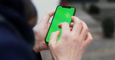 Close up of a mobile phone with a green screen in the hands of an unknown man scrolling the screen. Mockup, copy space, view from behind a man. in 4k, red komodo photo
