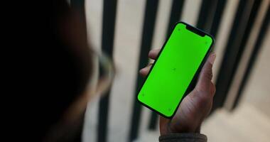 A mobile phone with a green screen in the hand of a man with glasses, close up, filming from behind, the face is not visible. Copy space, mockup, chroma key. in 4k, red komodo photo
