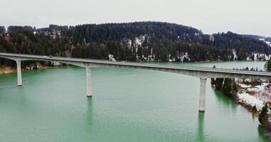 Beautiful winter landscape from bird's eye view, from a quadcopter. View of wide river flowing among spruce forests and fields covered with snow and narrow concrete road bridge connecting the banks photo