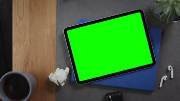 A man puts a cup of tea on the desktop next to a digital tablet with a green screen lying on a notepad with crumpled pieces of paper nearby, top view, close up. Mockup, chroma key, copy space photo