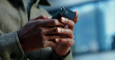 A man of African American appearance uses a mobile phone, standing near a building in which lamps shine in the windows. Close up of male hands with a phone, no face. in 4k, red komodo photo