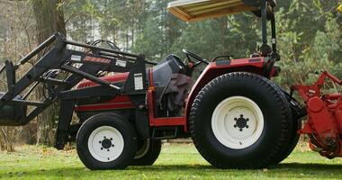 A modern agricultural tractor with a canopy above the driver's seat, with a bucket in front, stands at the edge of a field near the forest, close up photo