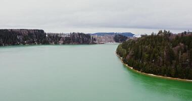 Beautiful winter landscape from bird's eye view. View of a wide river with small ripples of waves flowing through spruce forests and fields covered with snow. recording from a drone photo