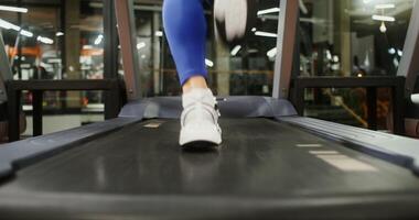 Close up of female legs in sneakers running on a treadmill, rear view. Beautiful footage of training on exercise equipment in the gym photo
