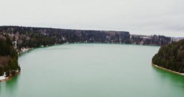 Vertical panning from a quadcopter, a view of a wide river flowing among spruce forests and snow covered fields. photo