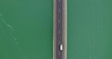 View from above, narrow road bridge with cars passing over it, over a river with green water with small ripples of waves. recording from a quadcopter photo