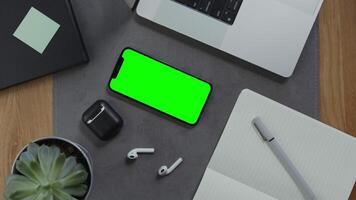 A man is going to take notes in a notebook lying next to a mobile phone with a green screen on the desktop, close up of male hands. Mockup, chroma key, copy space photo