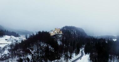 Medieval castle fortress on top of a hill overgrown with spruce forest on a winter snowy day. Close up shooting from a drone . Germany photo