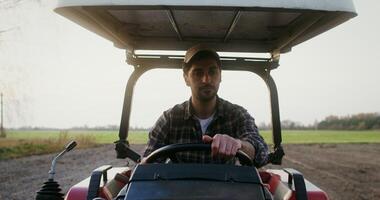 Close up front view of a tractor driver a young man of European appearance, with black hair and a beard with a serious view sitting at the wheel of an agricultural machine photo