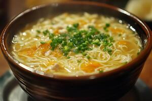Steaming chicken noodle soup garnished with chopped chives in brown bowl photo