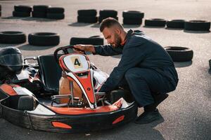 Technician, is ,,looking at the vehicle. Man is outdoors, kart racing conception photo