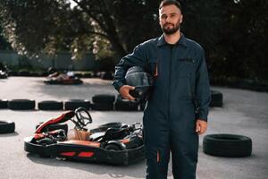 Standing and ,holding safety helmet. Man is outdoors, kart racing conception photo