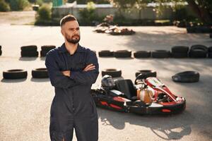 Standing,, with arms crossed. Man is outdoors, kart racing conception photo