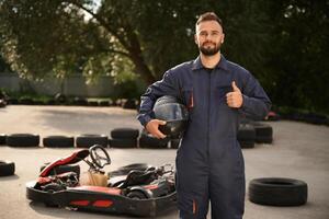 Standing, and holding safety helmet. Man is outdoors, kart racing conception photo
