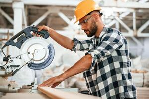 By the table,,, using blade, cutting the fresh wood. Industrial worker in warehouse photo