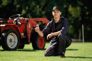 Sitting, with, thumb up. Man is, with utility tractor with grass cutter and aerator equipment on the field photo