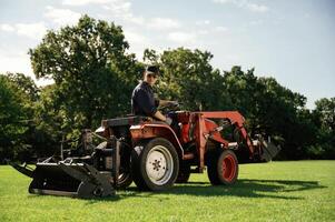Man is with utility ,tractor with grass cutter and aerator equipment on the field photo