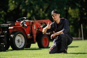 Sitting,, with, thumb ,up. Man is with utility tractor with grass cutter and aerator equipment on the field photo