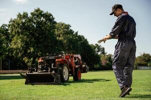 Rear, back view, walking... Man is with utility tractor with grass cutter and aerator equipment on the field photo