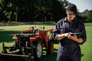 Black digital, tablet ,in hands. Man is with utility tractor with grass cutter and aerator equipment on the field photo