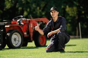 Sitting, with thumb,, up. Man is with utility tractor with grass cutter and aerator equipment on the field photo