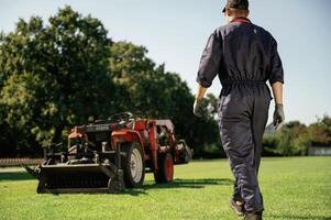 Rear, back, view, walking. Man is with utility tractor with grass cutter and aerator equipment on the field photo