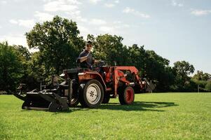 Man, is with ,utility tractor with grass cutter and aerator equipment on the field photo