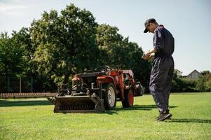 Rear,, back, view, walking. Man is with utility tractor with grass cutter and aerator equipment on the field photo