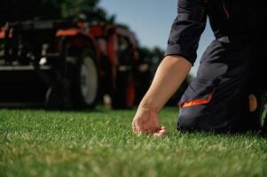 Quality control, touching ,the grass. Man is with utility tractor with grass cutter and aerator equipment on the field photo