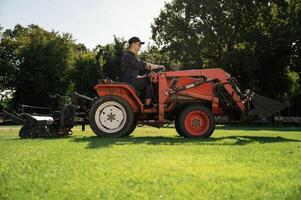 Man ,is, with utility tractor with grass cutter and aerator equipment on the field photo