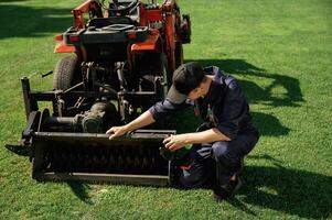 Checking the cutters. Man ,is ,with utility tractor with grass cutter and aerator equipment on the field photo