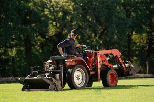 Sitting and driving. .Man is with utility tractor with grass cutter and aerator equipment on the field photo