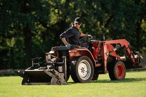 Sitting, and driving. Man is with utility tractor with grass cutter and aerator equipment on the field photo
