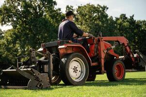 Sitting and ,driving. Man is with utility tractor with grass cutter and aerator equipment on the field photo