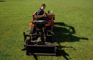Driving, looks, behind, shows thumb up. Man is with utility tractor with grass cutter and aerator equipment on the field photo
